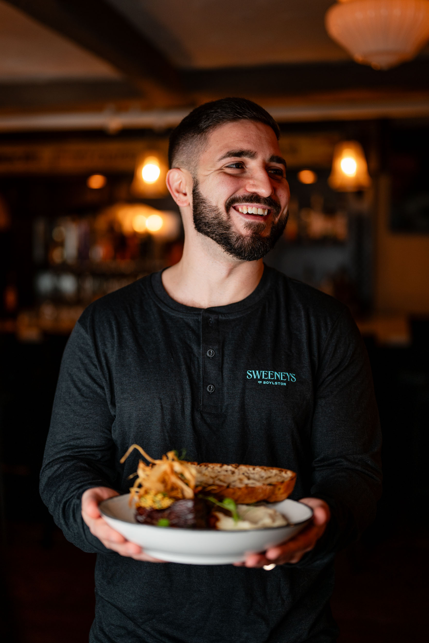 a server in a Sweeneys shirt smiles as he holds out the Guinness beef stew dish